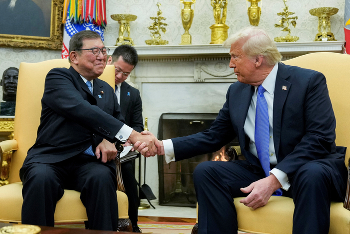 Presiden AS Donald Trump dan Perdana Menteri Jepang Shigeru Ishiba berjabat tangan dengan ekspresi tegang, dengan bendera Amerika Serikat dan Jepang sebagai latar belakang, merepresentasikan krisis hubungan AS-Jepang.